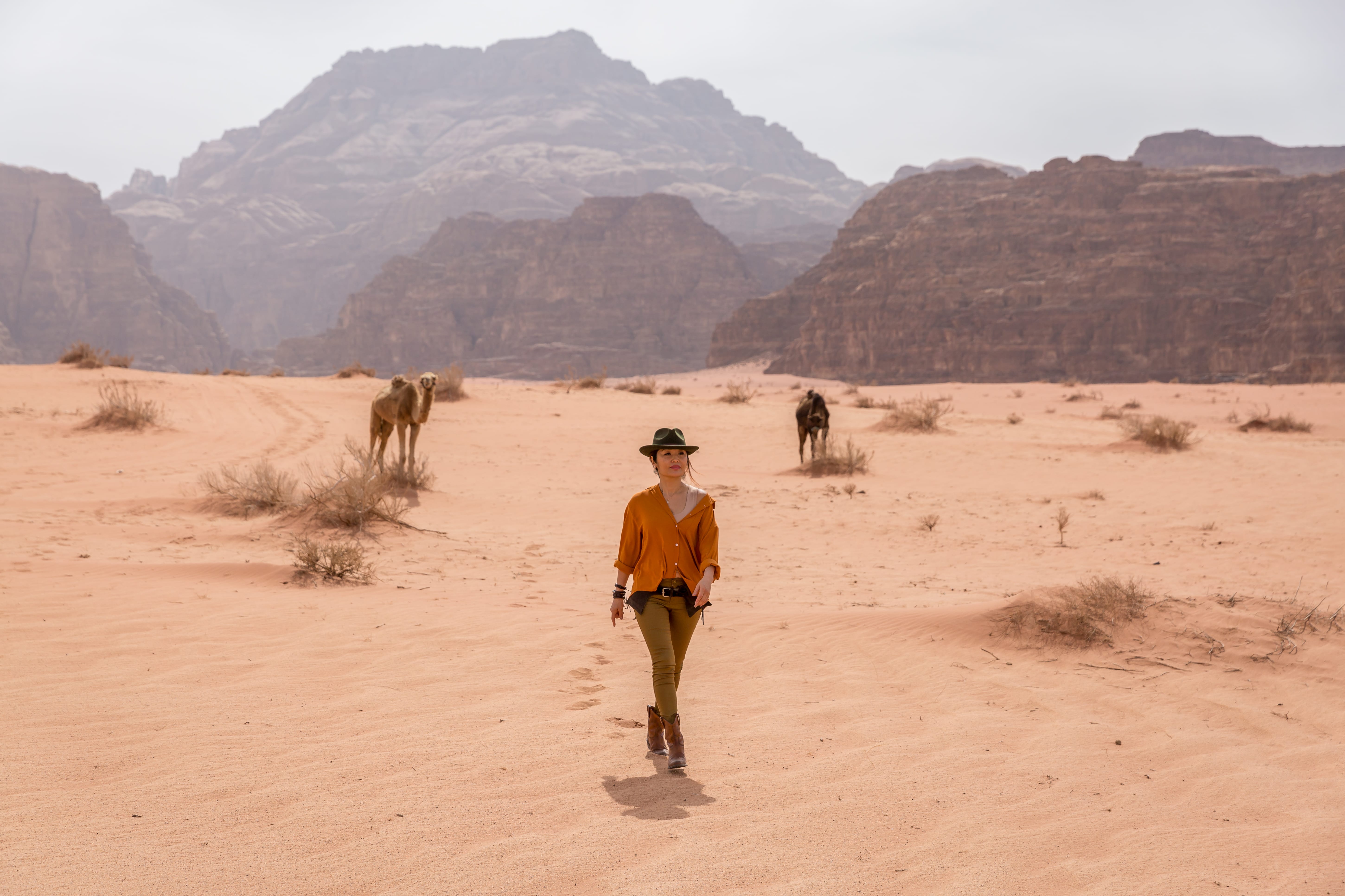 Девушка идёт по пустыне Вади Рам на фоне гор и верблюдов
