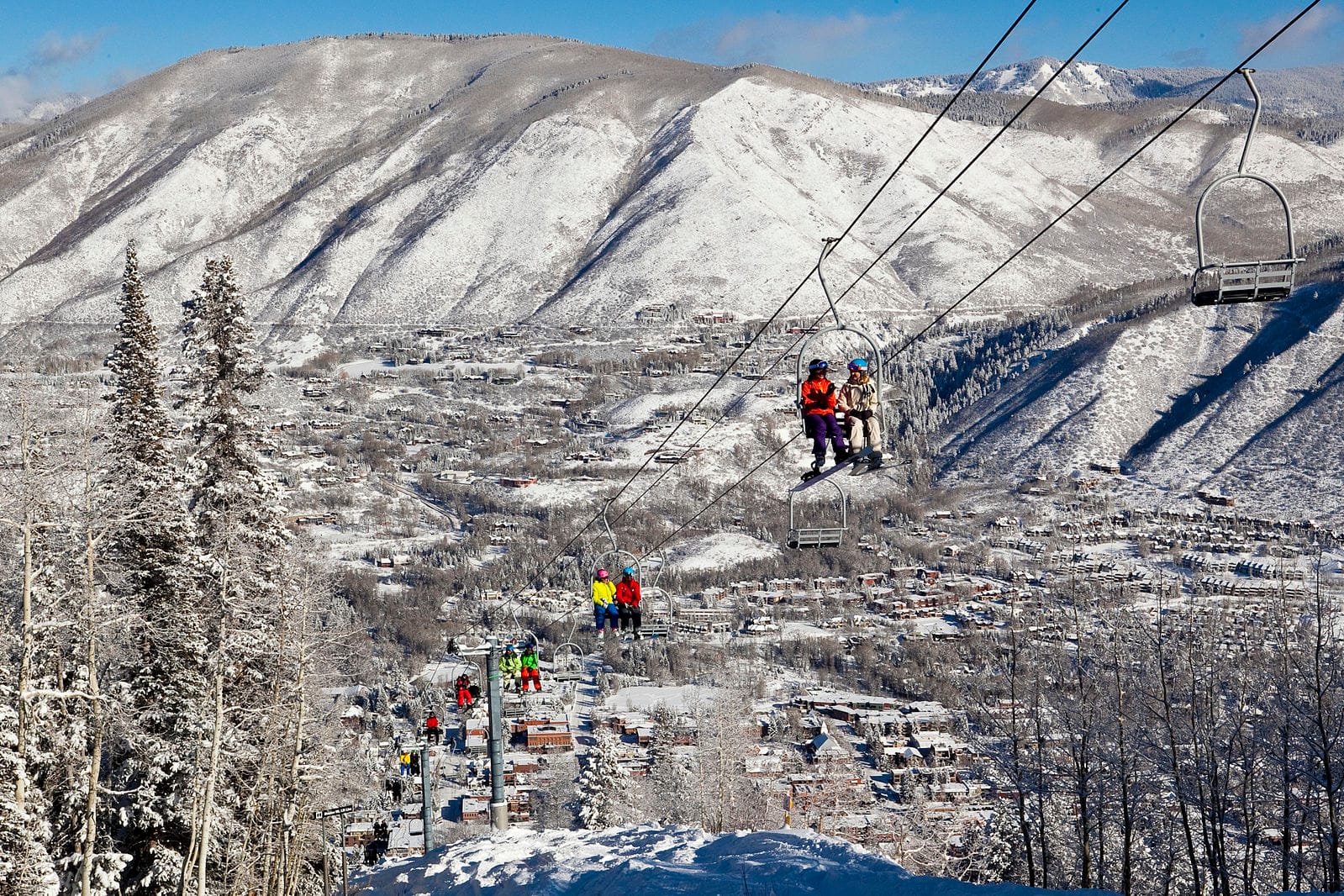Лыжники и сноубордисты поднимаются на легендарном подъемнике 1А на фоне горнолыжного курорта Аспен