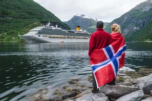 Пара с флагом Норвегии на берегу фьорда смотрит на круизный лайнер