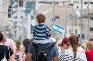 Отец и ребёнок с флагом в руке идут с толпой по Тель-Авиву в день независимости Израиля