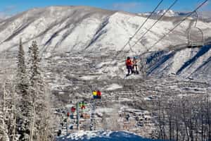 Лыжники и сноубордисты поднимаются на легендарном подъемнике 1А на фоне горнолыжного курорта Аспен